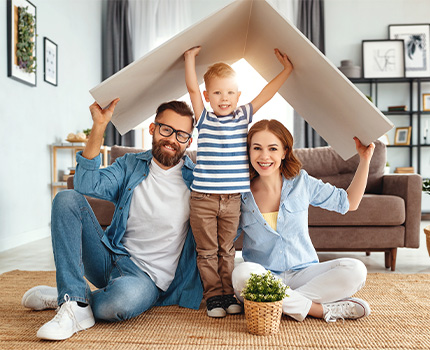 Famiglia felice in posa sotto cartone del tetto di una casa di carta fotografati nel loro salone. 