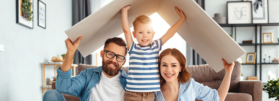 Famiglia felice in posa sotto cartone del tetto di una casa di carta fotografati nel loro salone. 