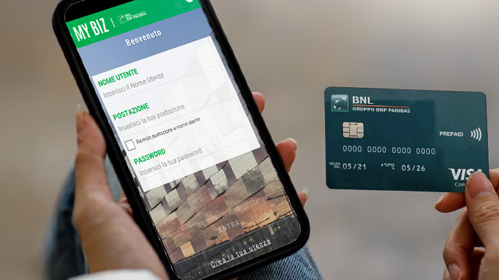 Uomo che tiene in mano uno smartphone con l'app My Biz aperta e nell'altra mano una Carta Prepagata Commercial