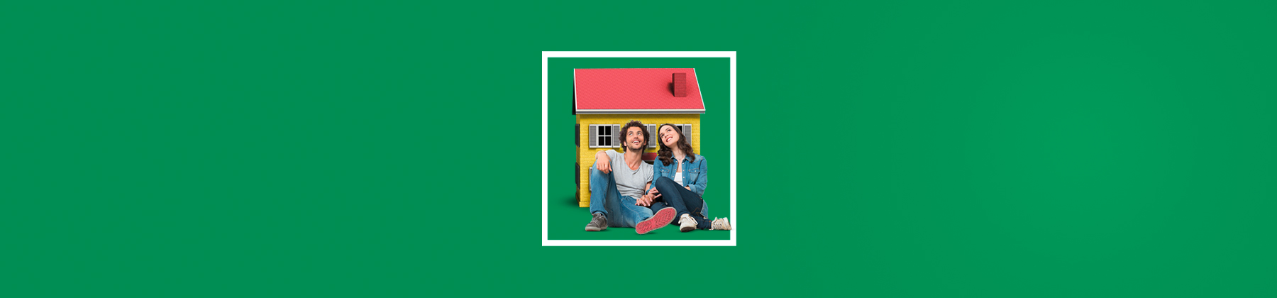 Un ragazzo e una ragazza seduti a terra si tengono per mano sorridenti, con la schiena poggiata su una casa troppo piccola