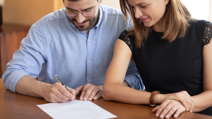  Uomo e donna sorridenti seduti a una scrivania firmano un documento.