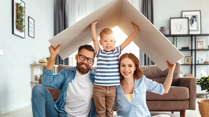 Famiglia di due genitori e un bambino nel loro salotto con un cartone a forma di tetto sulla casa. 