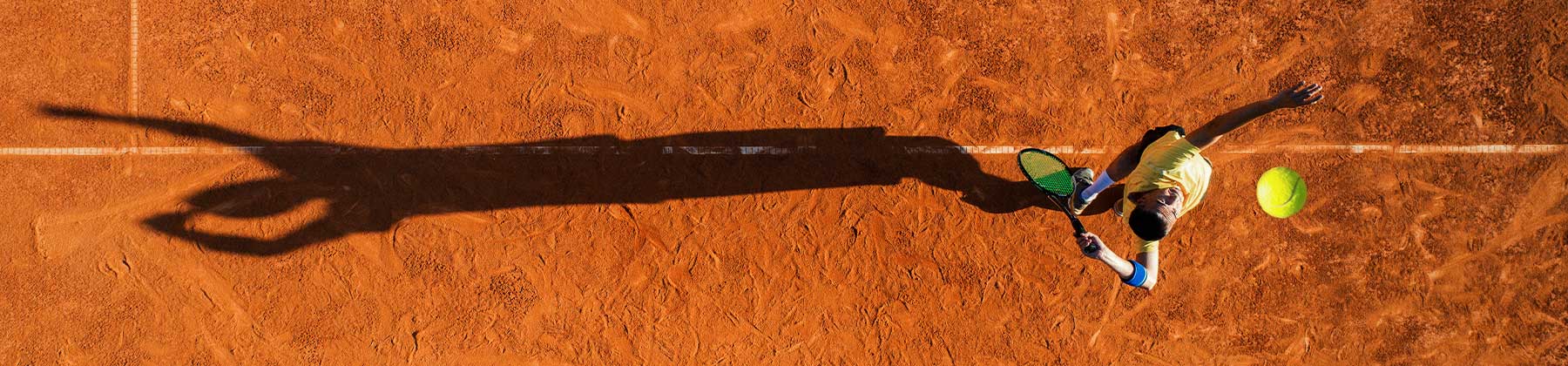 Foto aerae di un tennista che sta per servire su un campo di terra rossa.