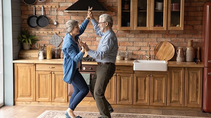 Coppia uomo e donna in età pensionabile accennano gioisamente un passo di danza nella loro nuova cucina