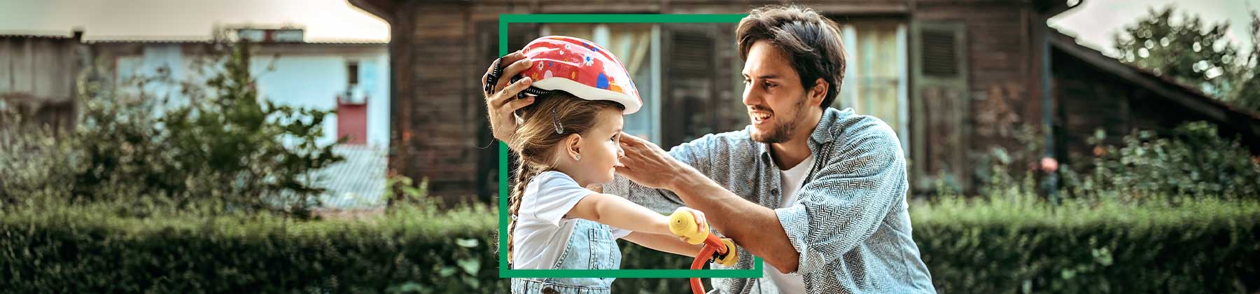 Immagine di un giovane uomo che sistema il caschetto a una bimba in bicicletta,