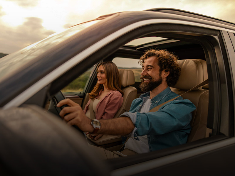 Uomo alla guida di un'auto e donna sorridente sul sedile del passeggero