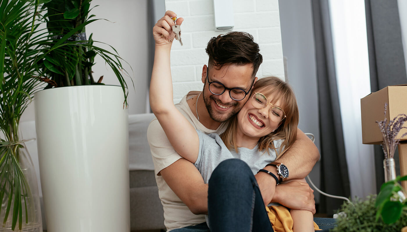Coppia giovane sorridente che si abbraccia con le chiavi di casa in mano.