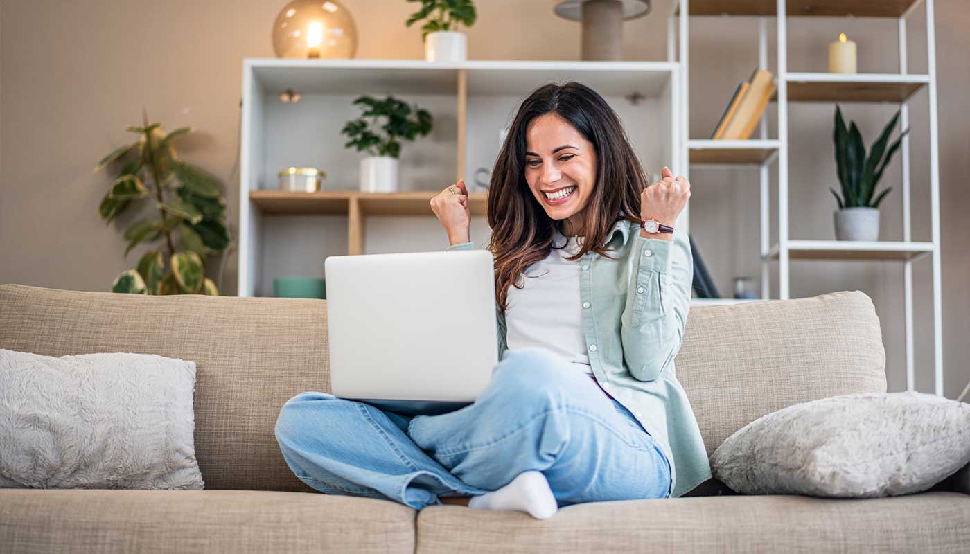Ragazza giovane sorridente sul divano con pc in grembo
