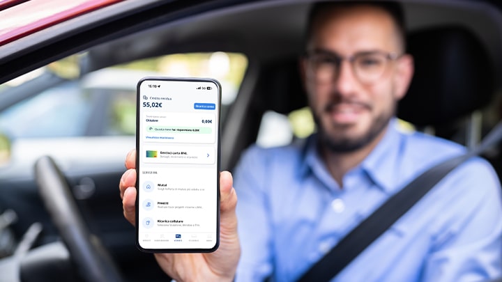 Un uomo alla guida di una autovettura mostra lo smartphone con la schermata del conto BNL nell'app Telepass Pay X