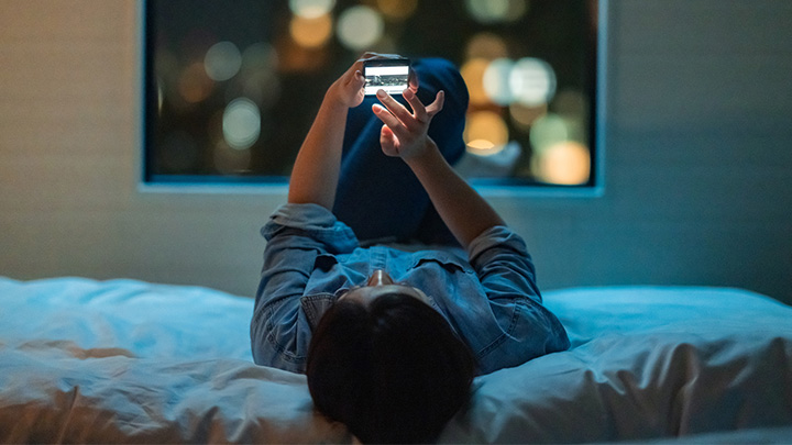 Donna distesa sul letto in relax con lo smartphone in mano 